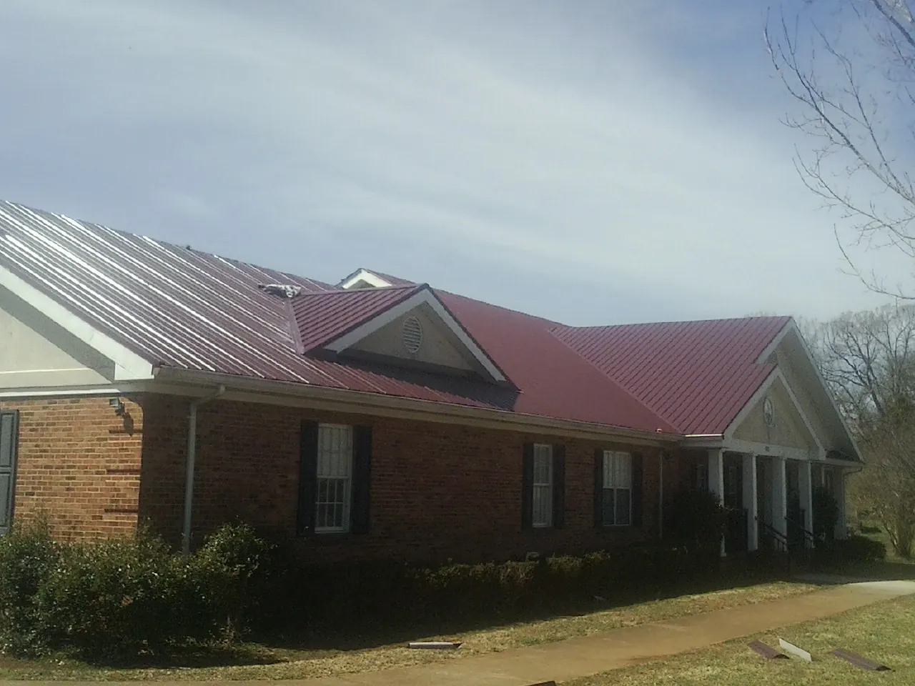 Red metal roof with gabled entries on a long brick building, from a Hail Damage Roof Repair job in Crawford